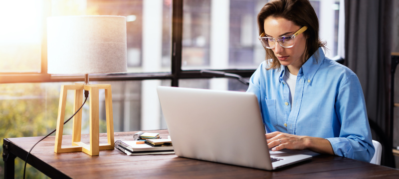 Young woman working with a laptop. Female freelancer connecting to internet via computer. Blogger or journalist writing new article.