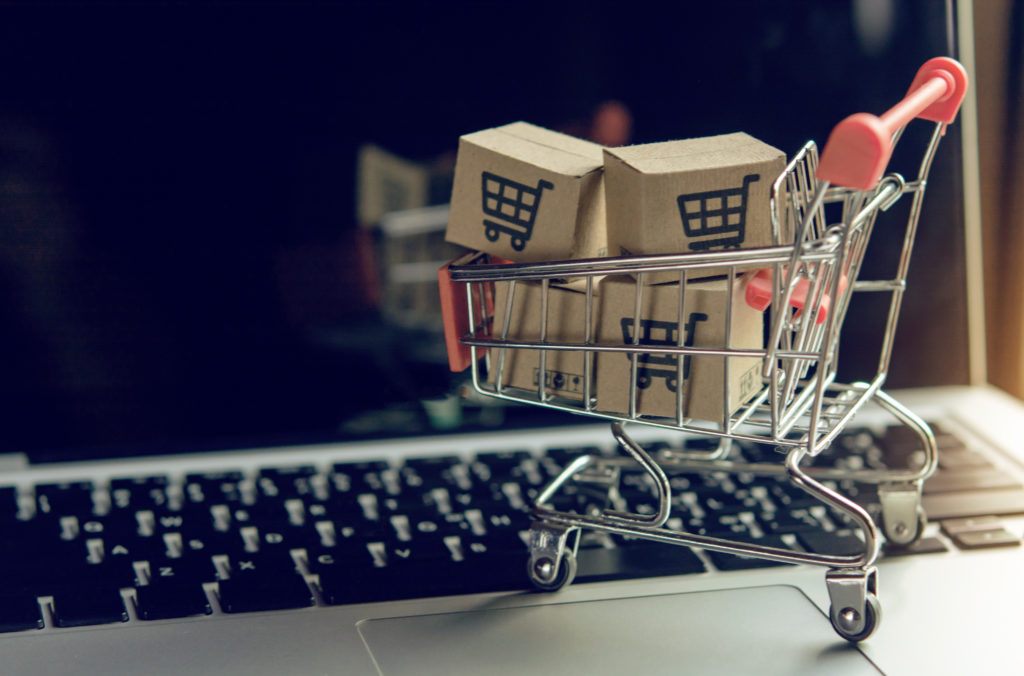 Shopping online concept - Parcel or Paper cartons with a shoppin Mini shopping cart with boxes next to a computer