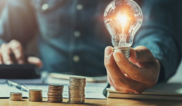 business man hand holding lightbulb with using calculator to calculate and money stack. idea saving energy and accounting finance in office concept